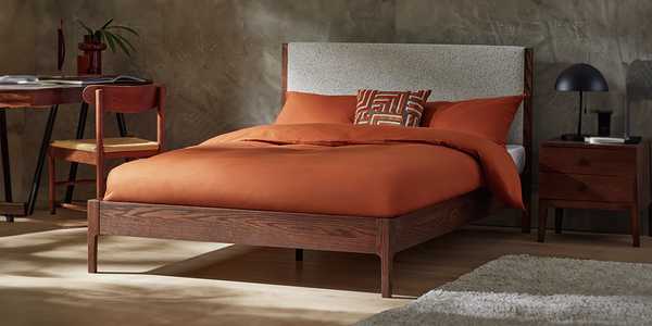Brown wooden bed frame with orange bedding and cushions.
